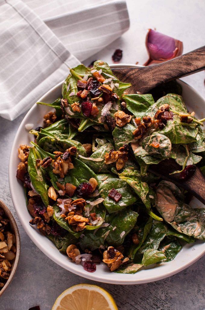bowl of spinach salad with pancetta and candied nuts with wooden salad utensils