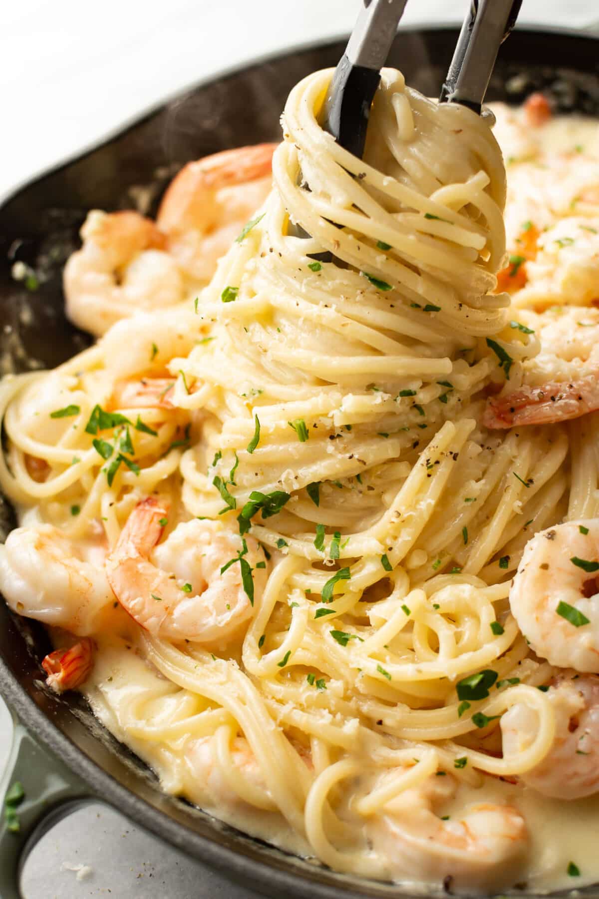 a skillet with creamy lemon shrimp pasta and cooking tongs