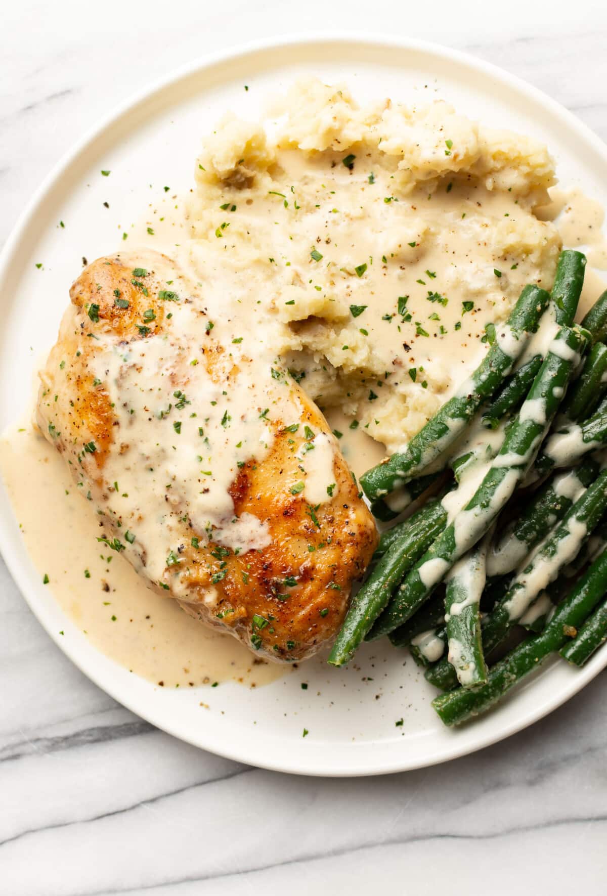 a plate with creamy lemon chicken, mashed potatoes, and green beans