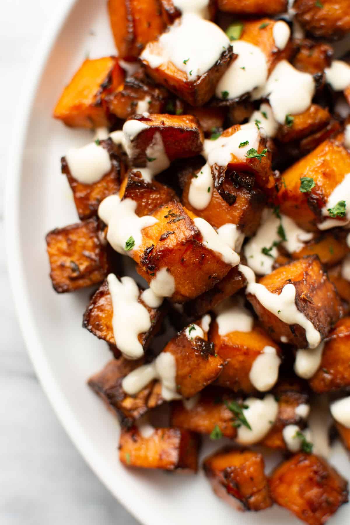 a bowl of roasted sweet potatoes with lemon tahini sauce drizzled over top