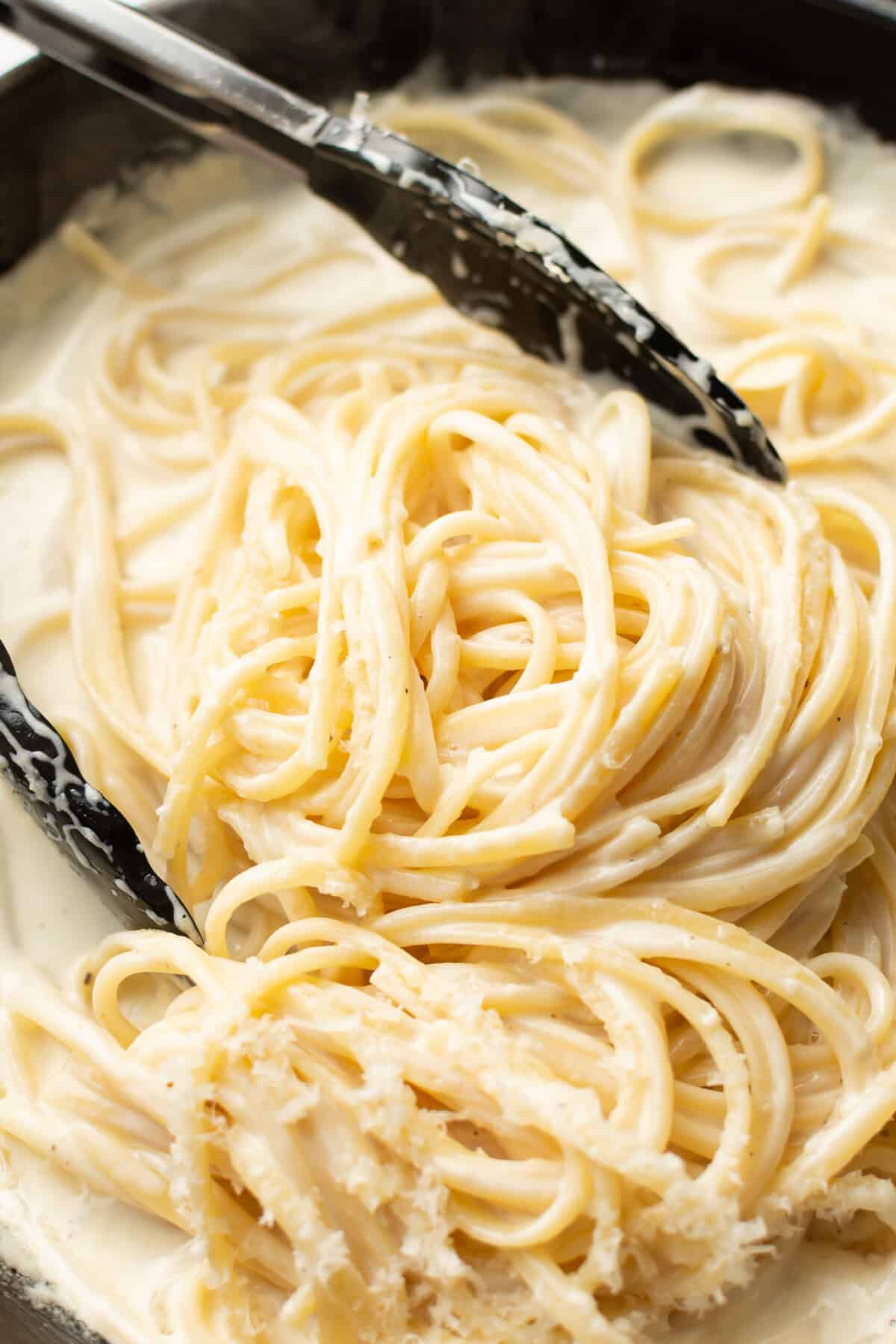 a skillet with creamy garlic pasta and kitchen tongs