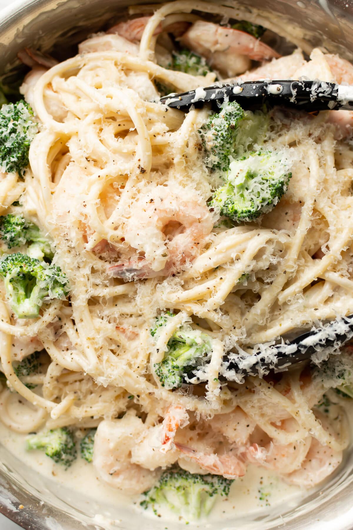 closeup of a skillet with shrimp and broccoli pasta and serving tongs