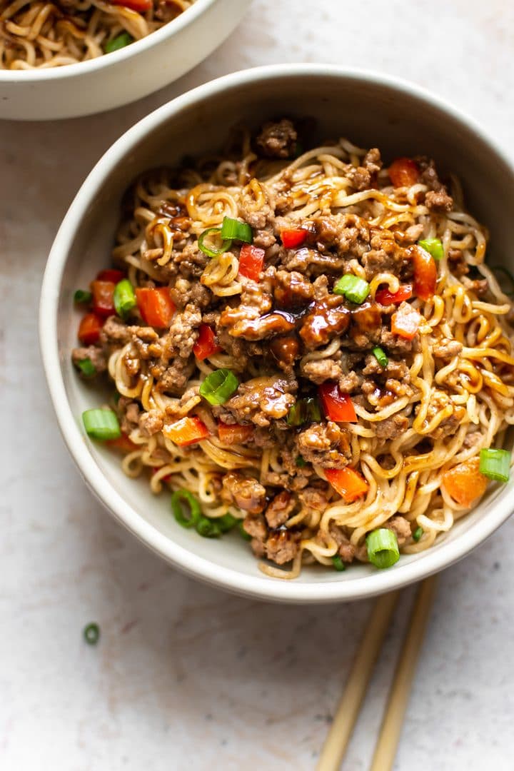 Asian beef noodles in a bowl with chopsticks, scallions, red peppers, and extra hoisin sauce