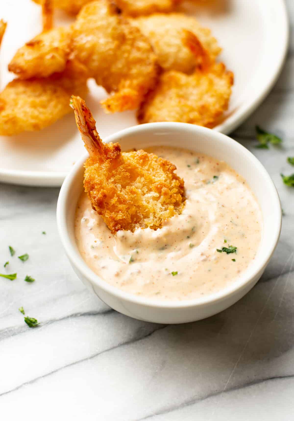 dipping breaded shrimp into a bowl of remoulade sauce