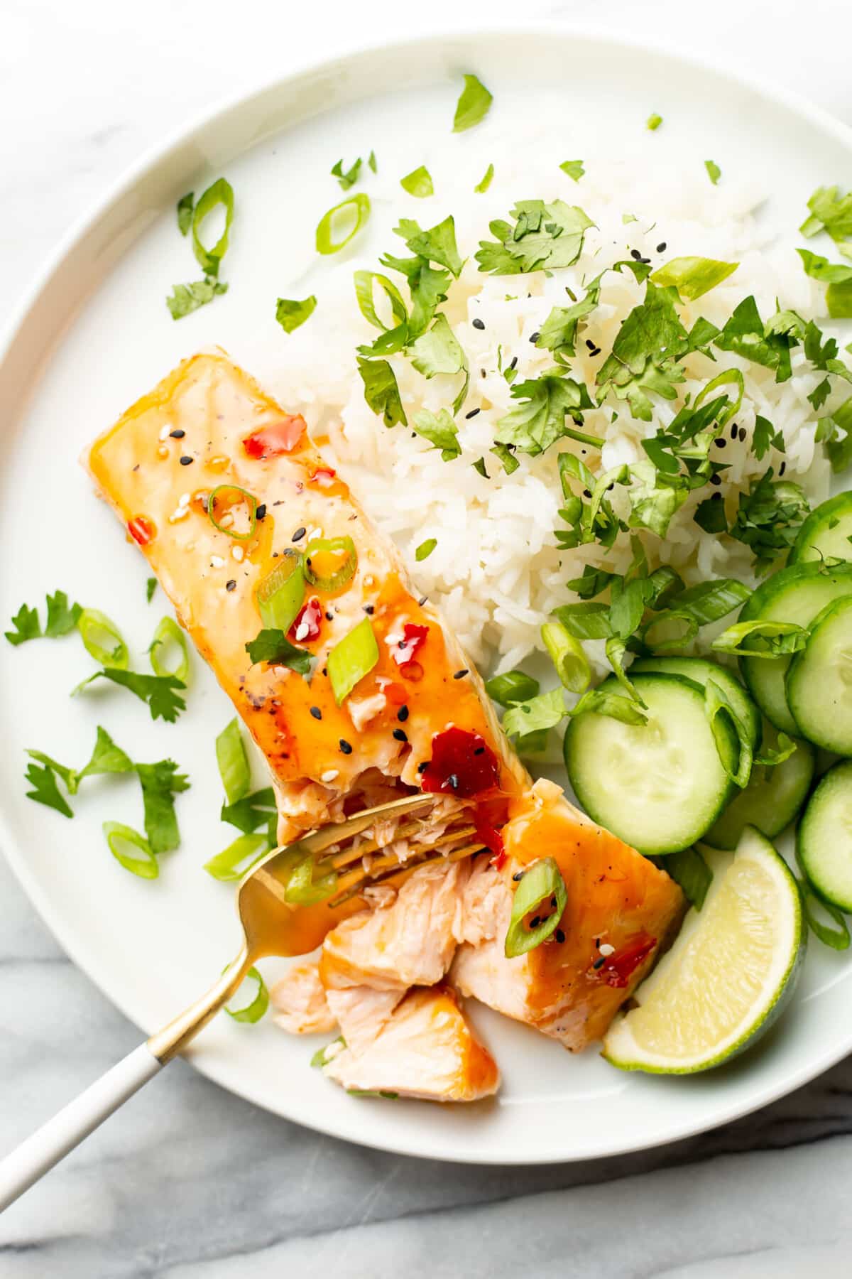 a plate with sweet chili salmon, rice, and cucumbers with a fork