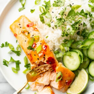 a plate with sweet chili salmon, rice, and cucumbers with a fork