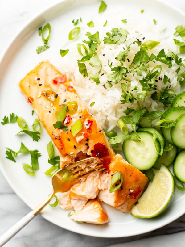 a plate with sweet chili salmon, rice, and cucumbers with a fork