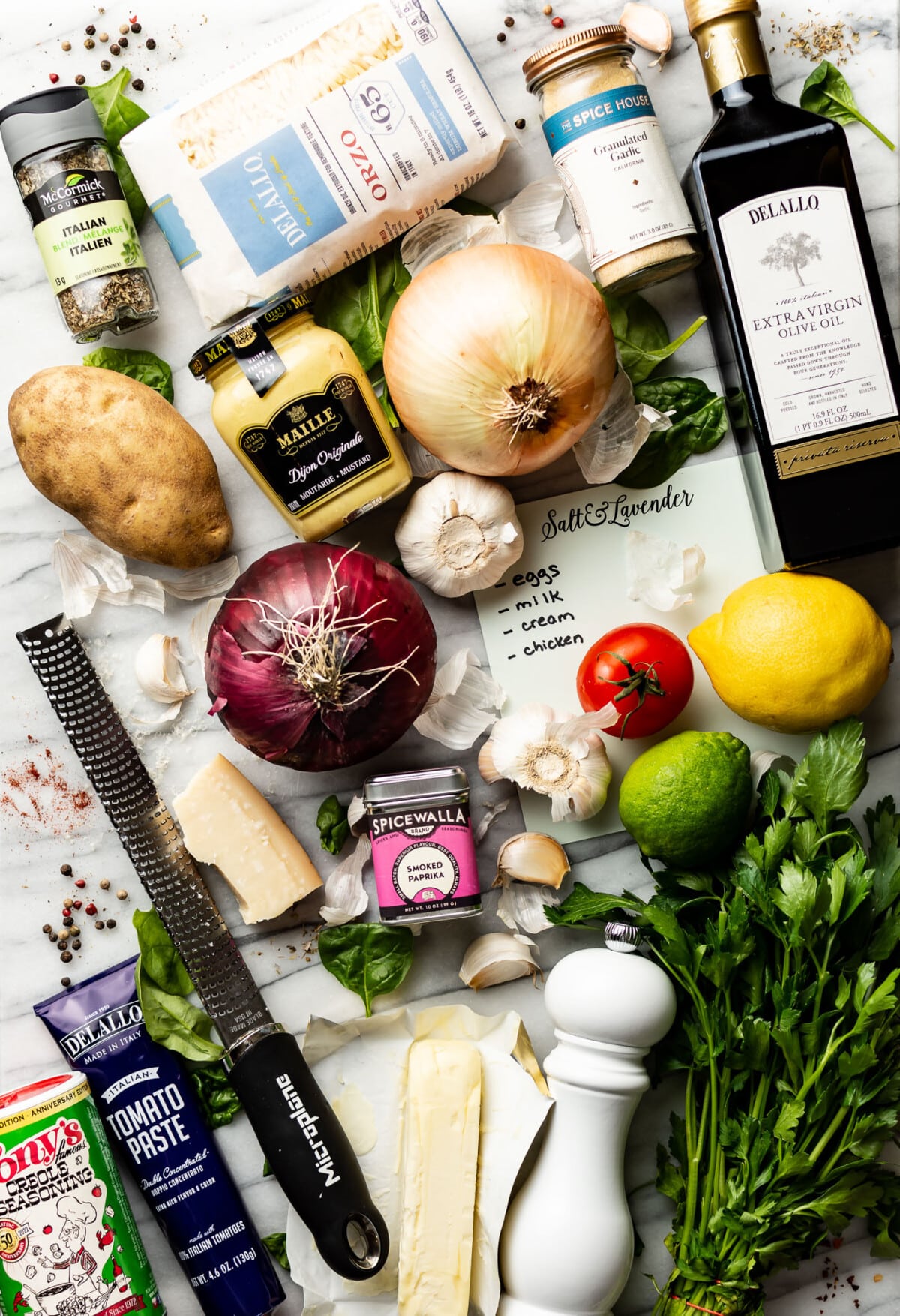 many kitchen essentials on a counter including oil, garlic, onions, lemons, pasta, and kitchen tools