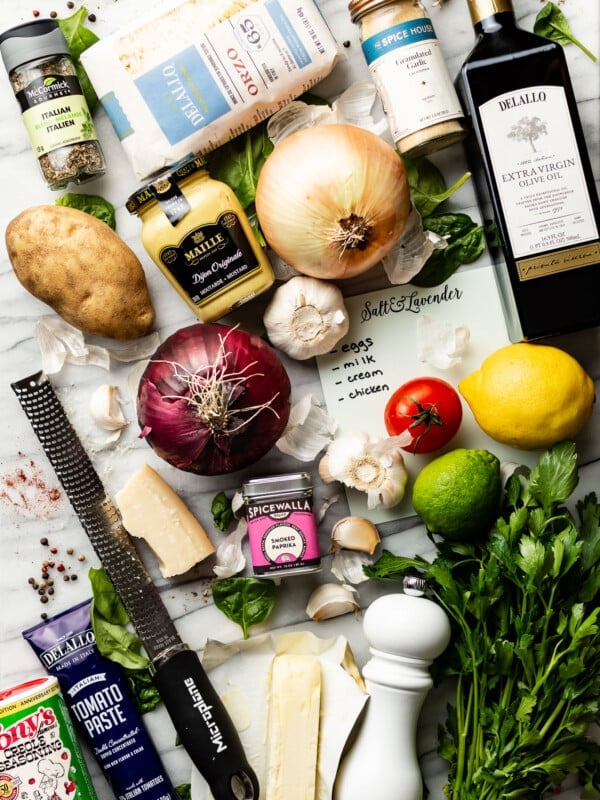 many kitchen essentials on a counter including oil, garlic, onions, lemons, pasta, and kitchen tools