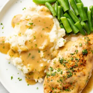 a plate with ranch chicken and gravy, green beans, and mashed potatoes