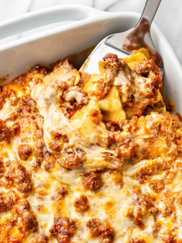 baking dish with cheesy baked ravioli and metal spatula