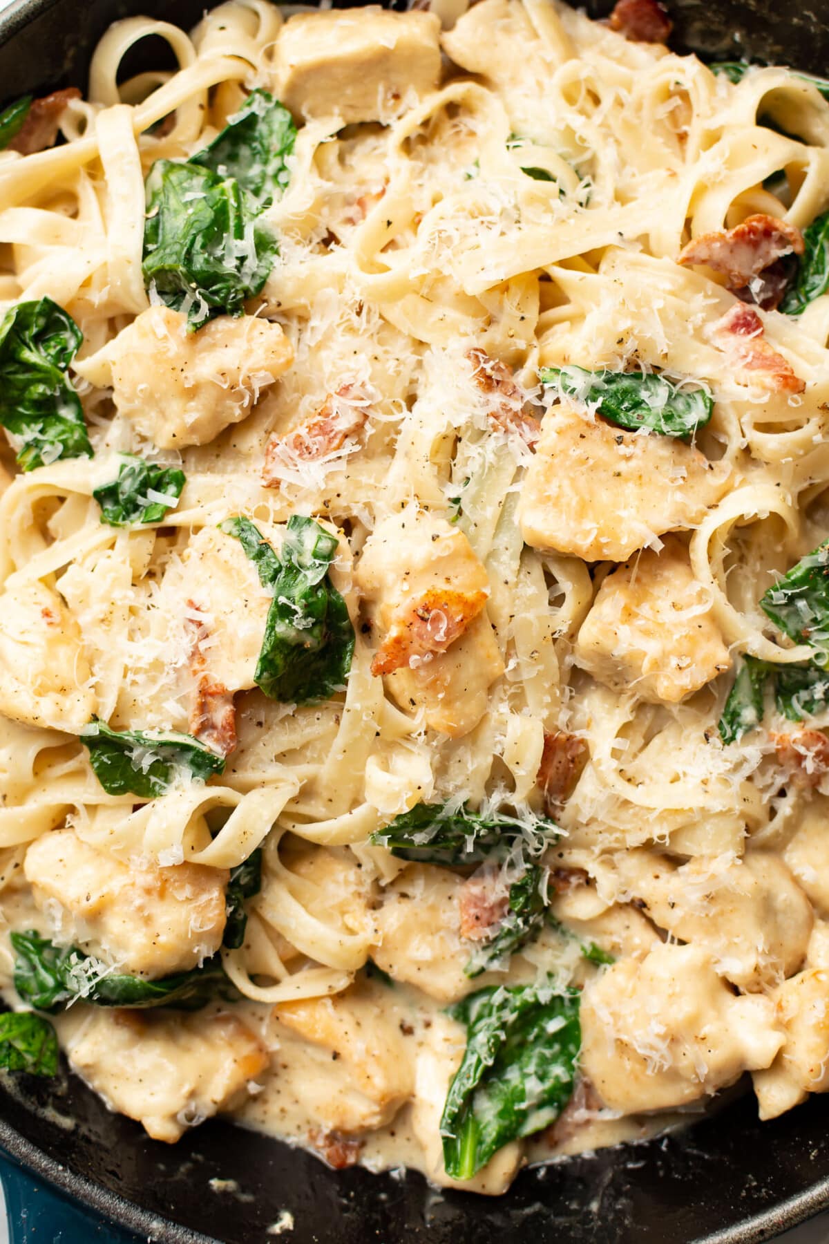 closeup of a skillet with creamy chicken bacon spinach fettuccine and parmesan