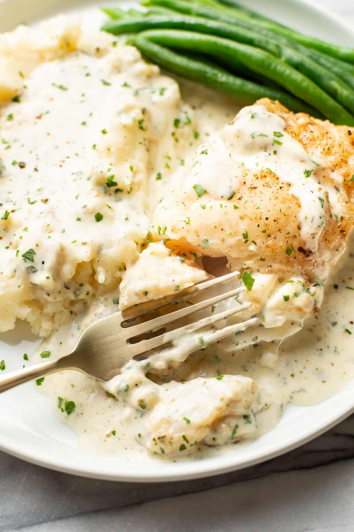 a plate with creamy lemon parmesan cod, mashed potatoes, and green beans