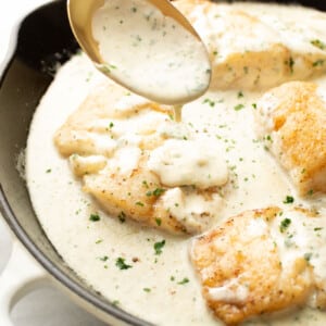 a skillet with creamy lemon parmesan cod and a serving spoon