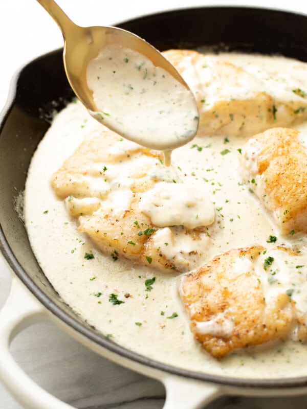 a skillet with creamy lemon parmesan cod and a serving spoon