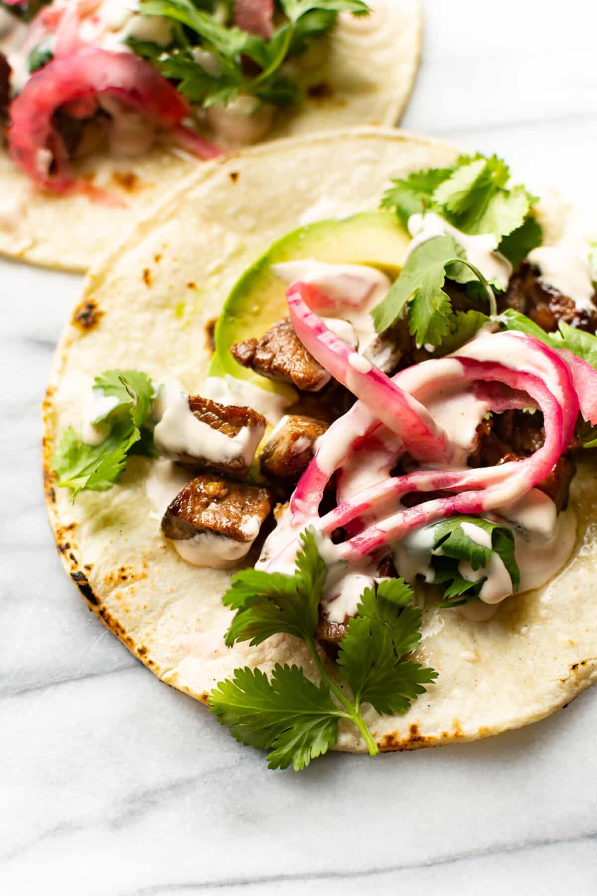 two steak tacos on a marble surface