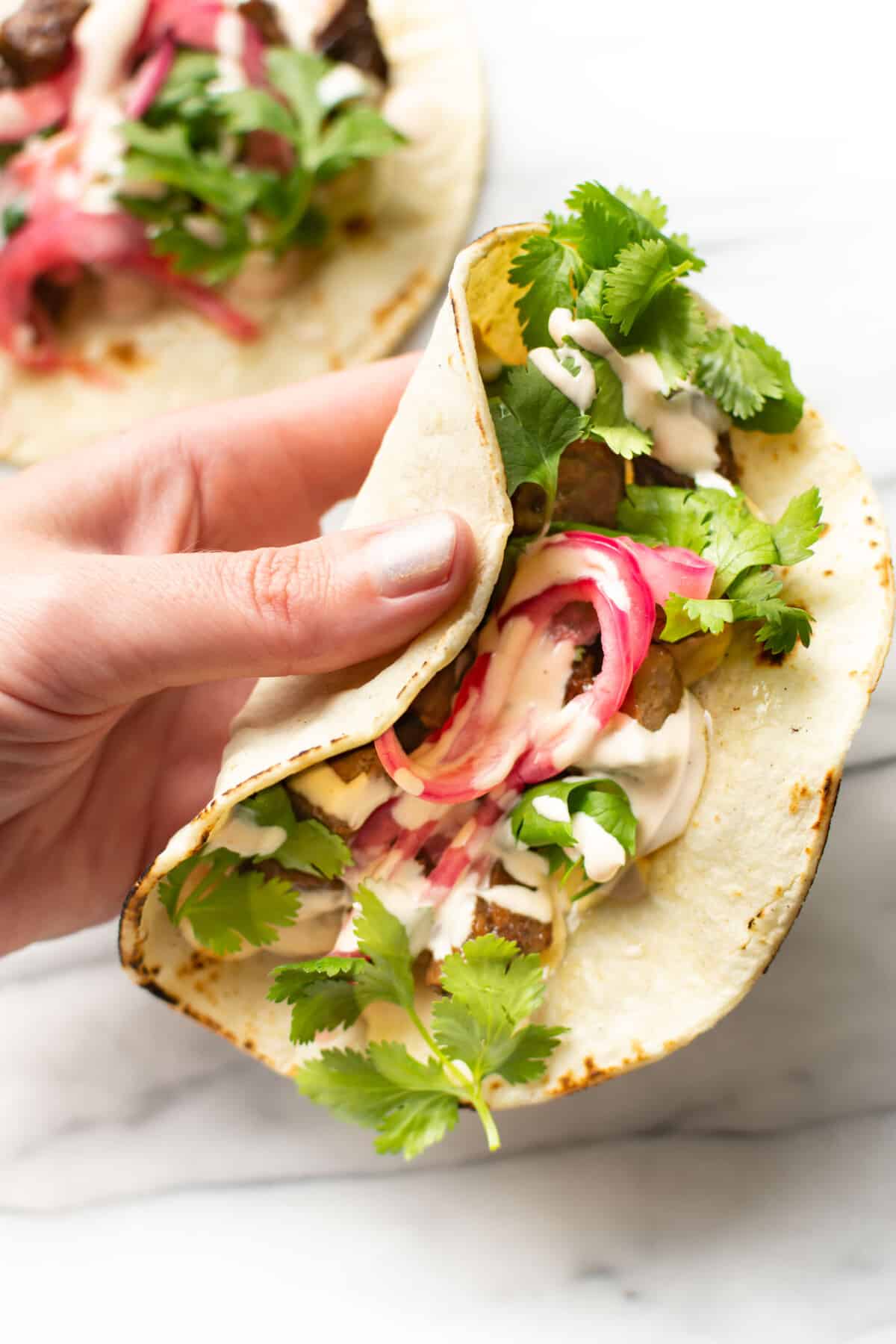 a hand holding a steak taco with creamy chipotle lime sauce