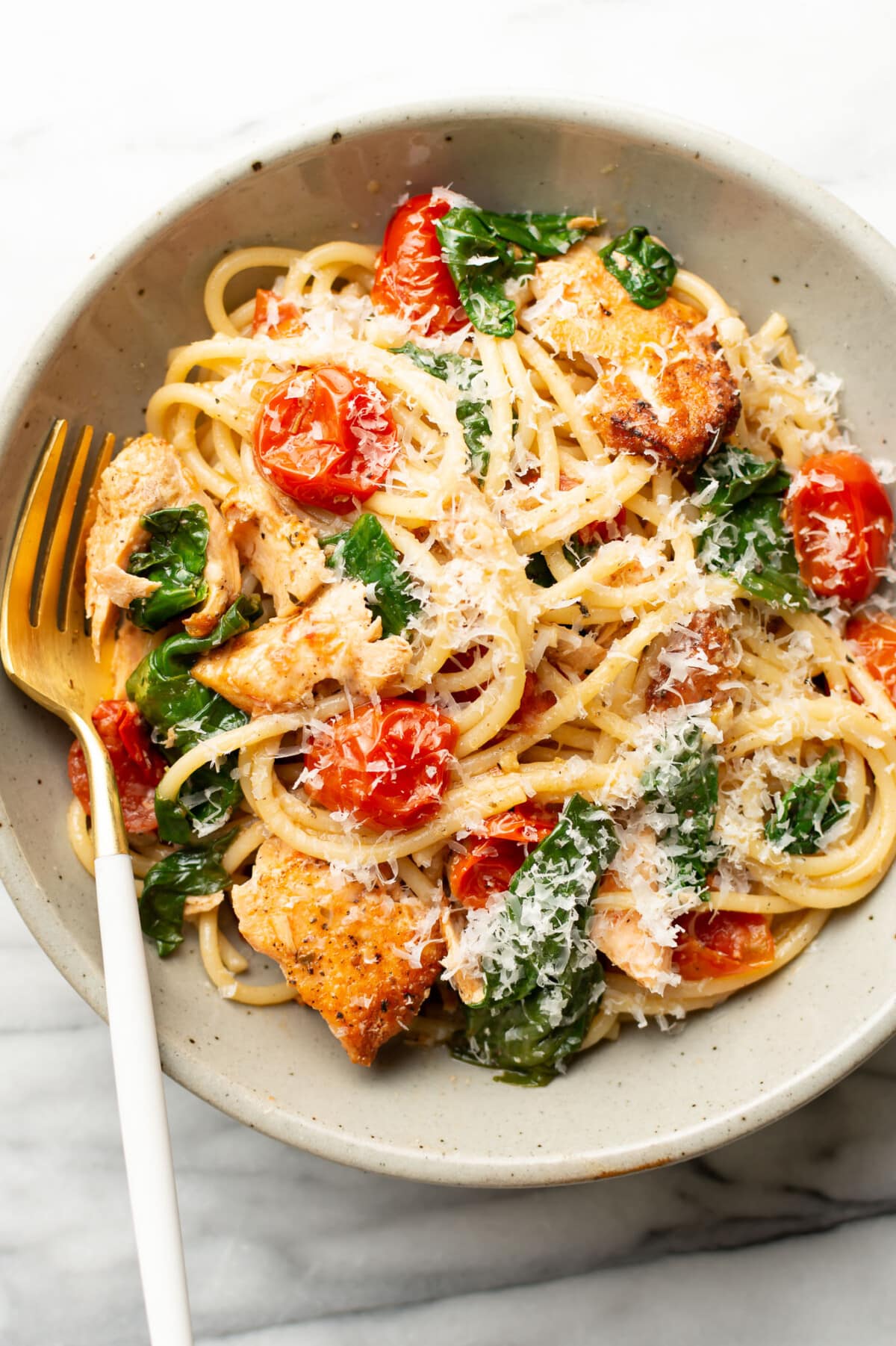 a bowl of tomato spinach salmon pasta with a fork