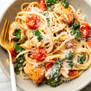 a bowl of tomato spinach salmon pasta with a fork