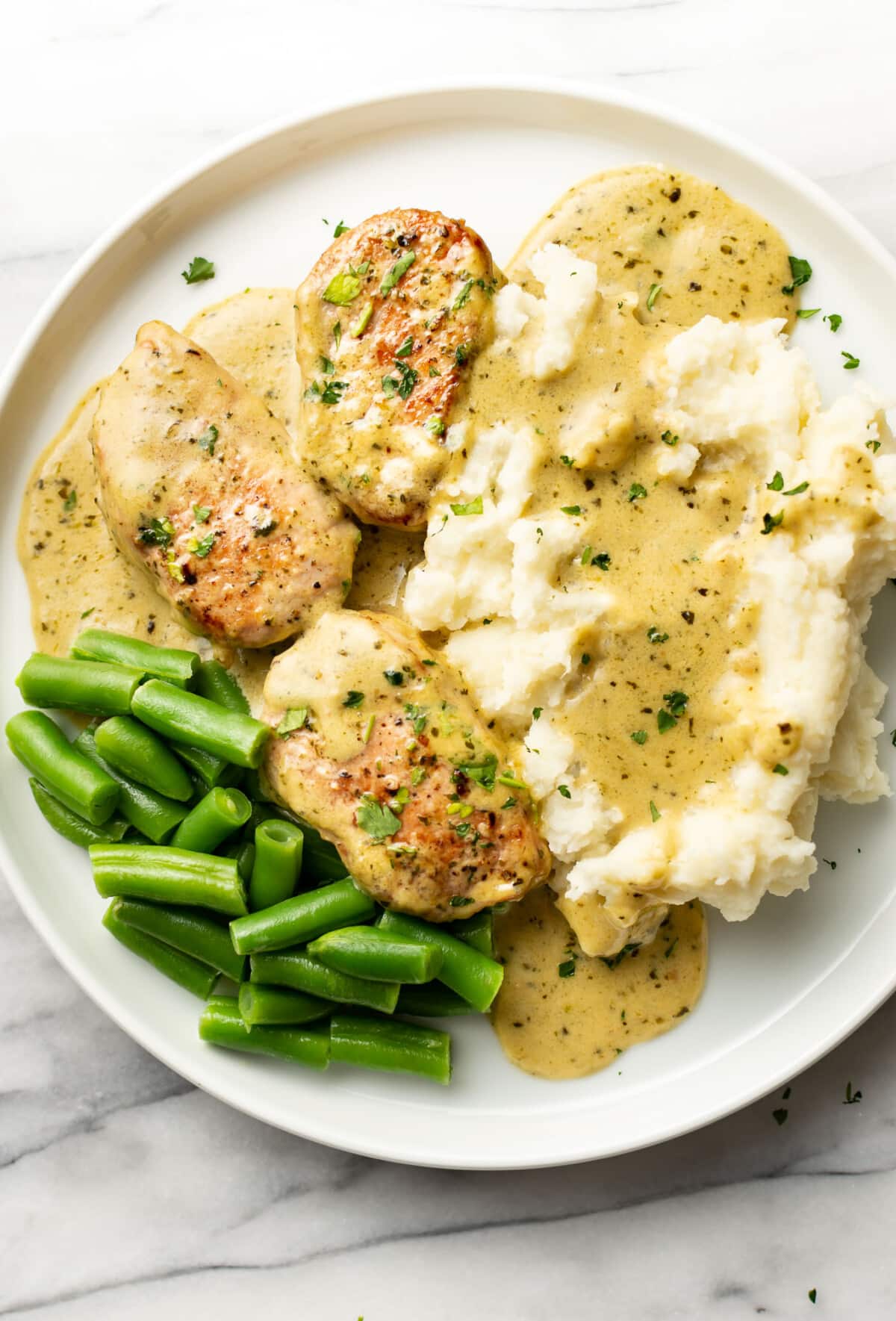 a plate with pesto pork tenderloin, mashed potatoes, and green beans