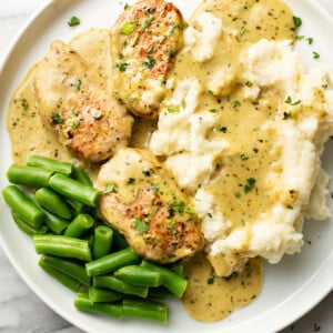 a plate with pesto pork tenderloin, mashed potatoes, and green beans