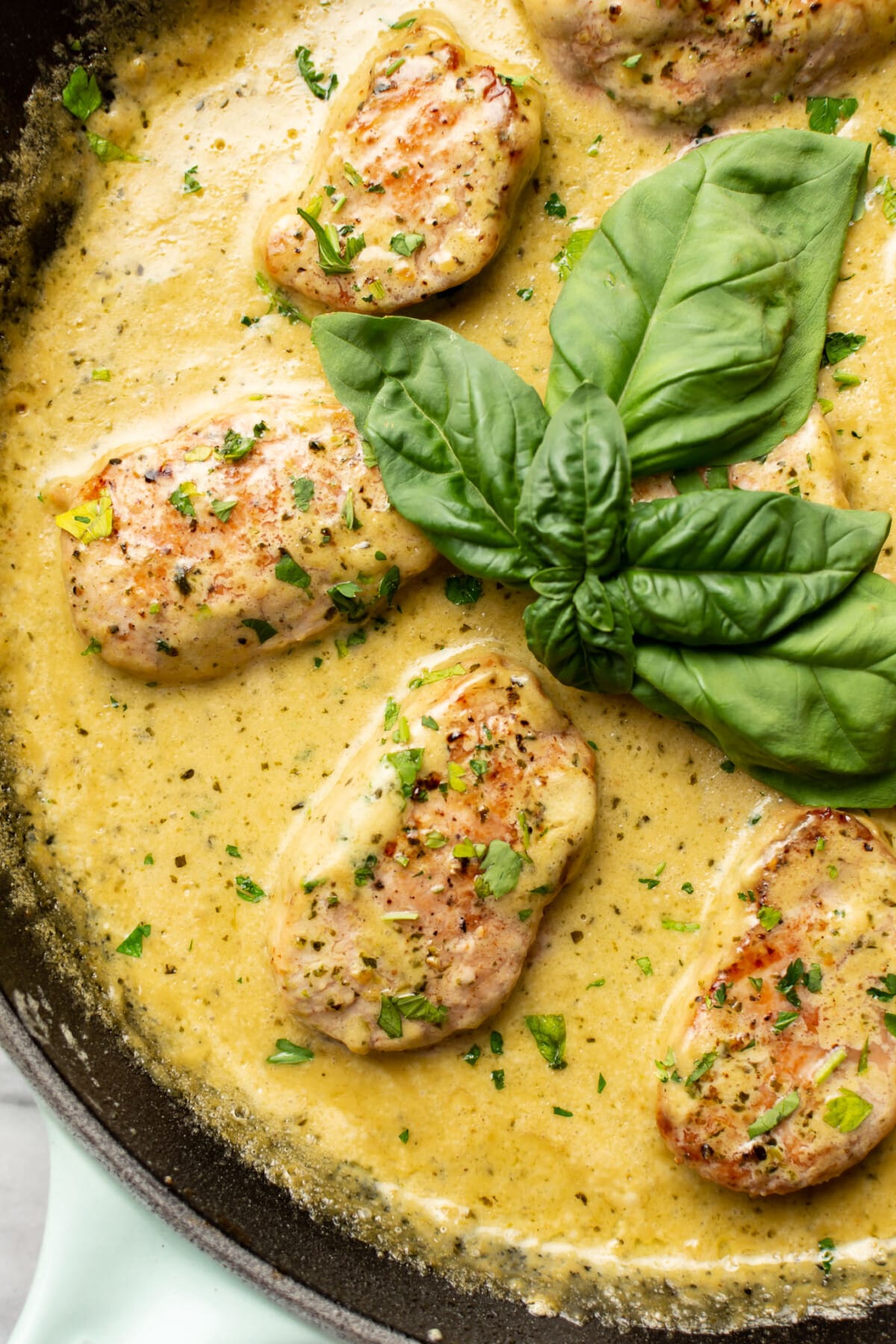 a skillet with pork tenderloin medallions in pesto sauce with basil