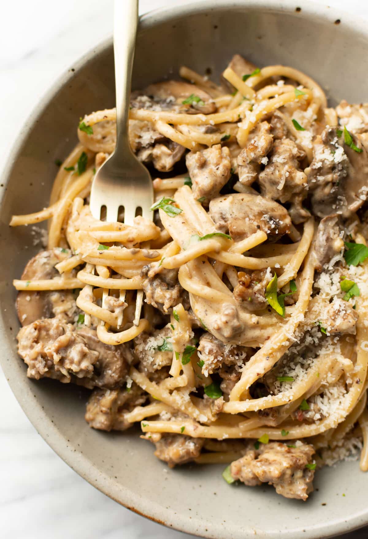 a bowl of italian sausage and mushroom pasta with a fork
