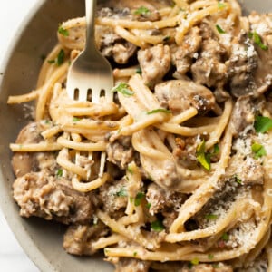 a bowl of italian sausage and mushroom pasta with a fork