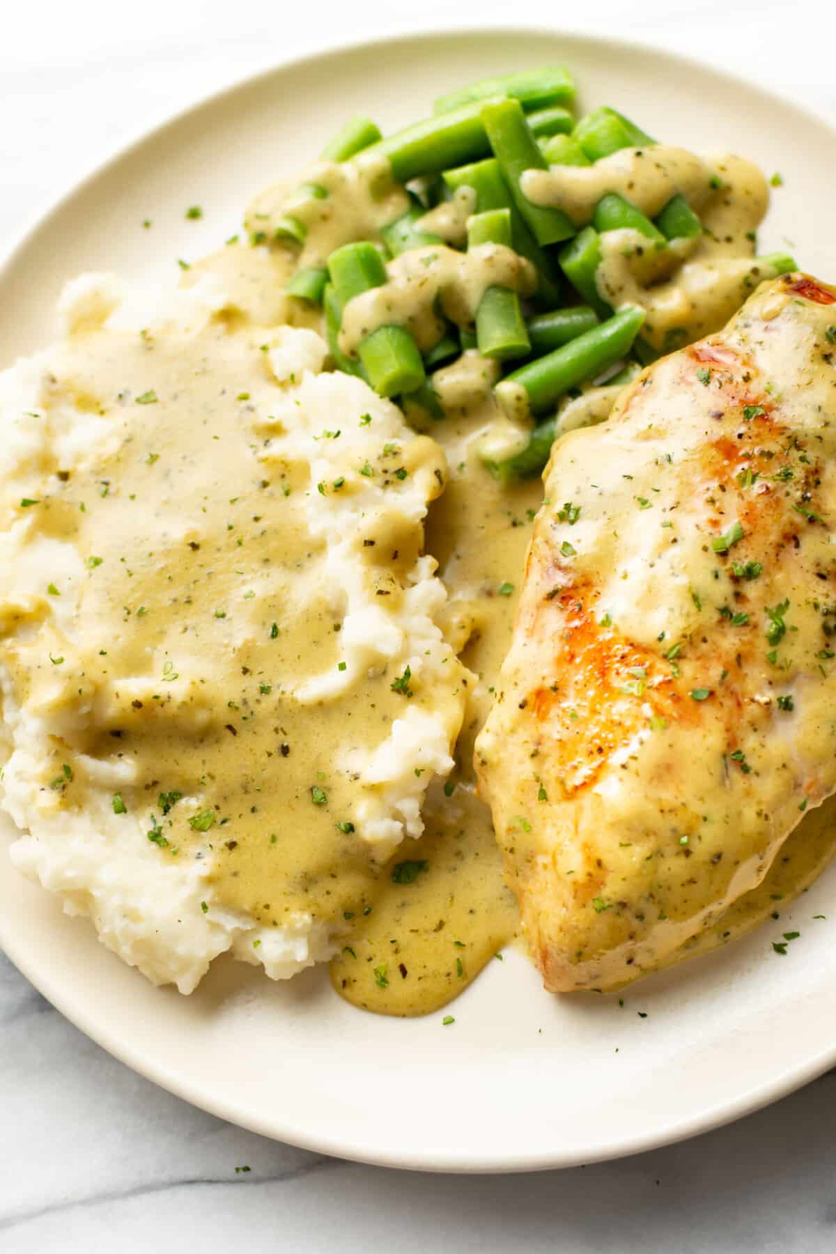 a plate with creamy pesto chicken, mashed potatoes, and green beans