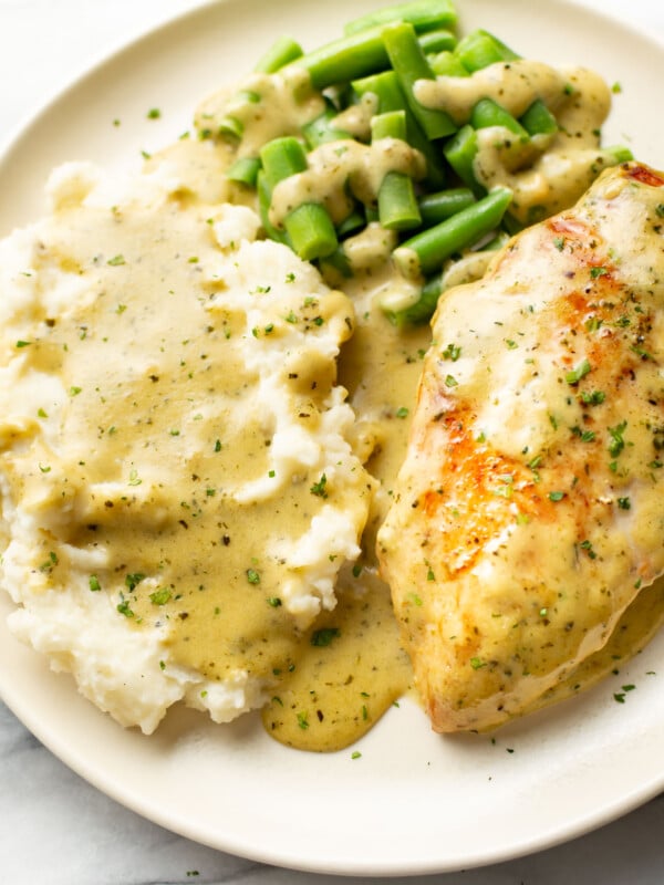 a plate with creamy pesto chicken, mashed potatoes, and green beans