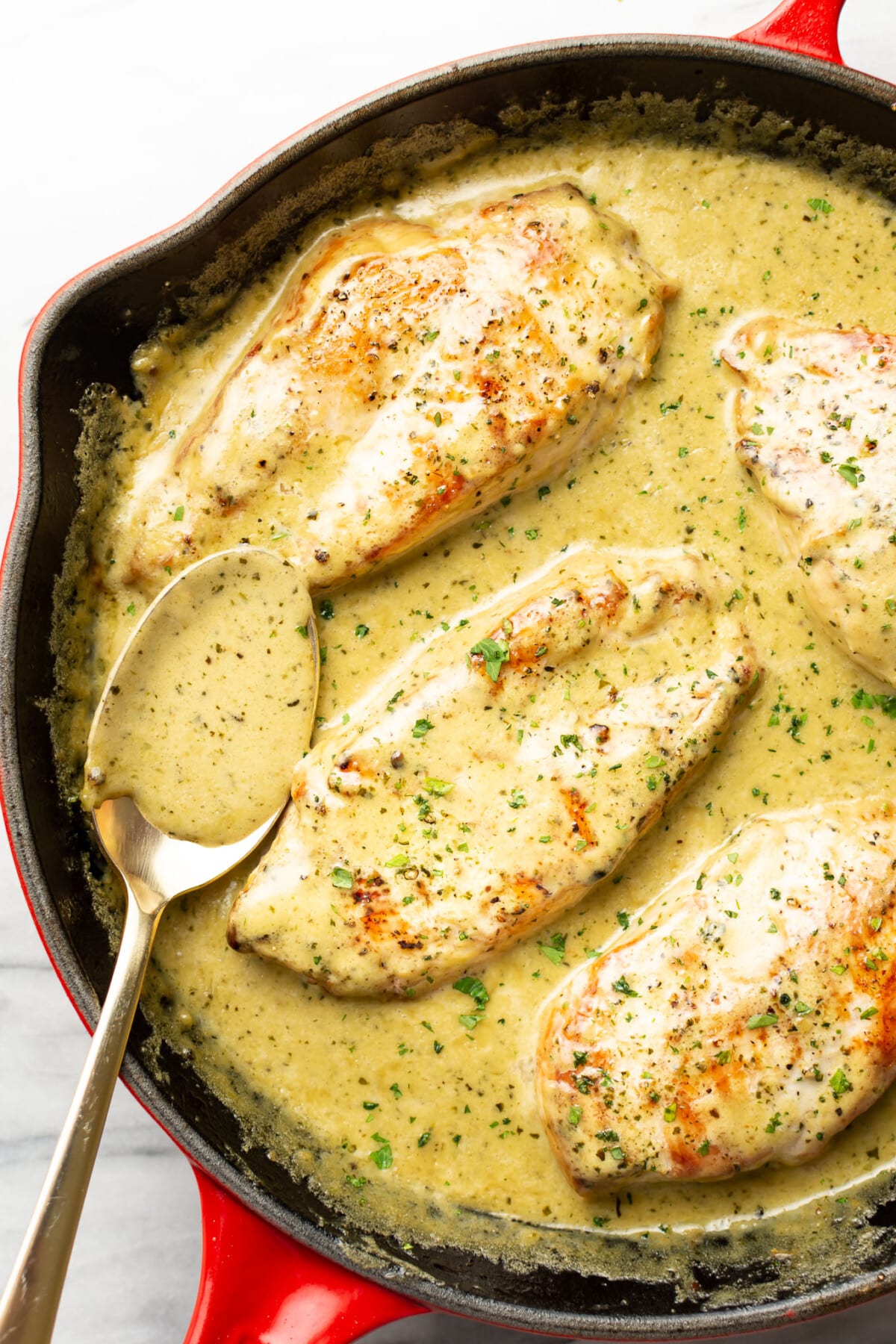 a skillet with chicken in creamy pesto sauce with a serving spoon