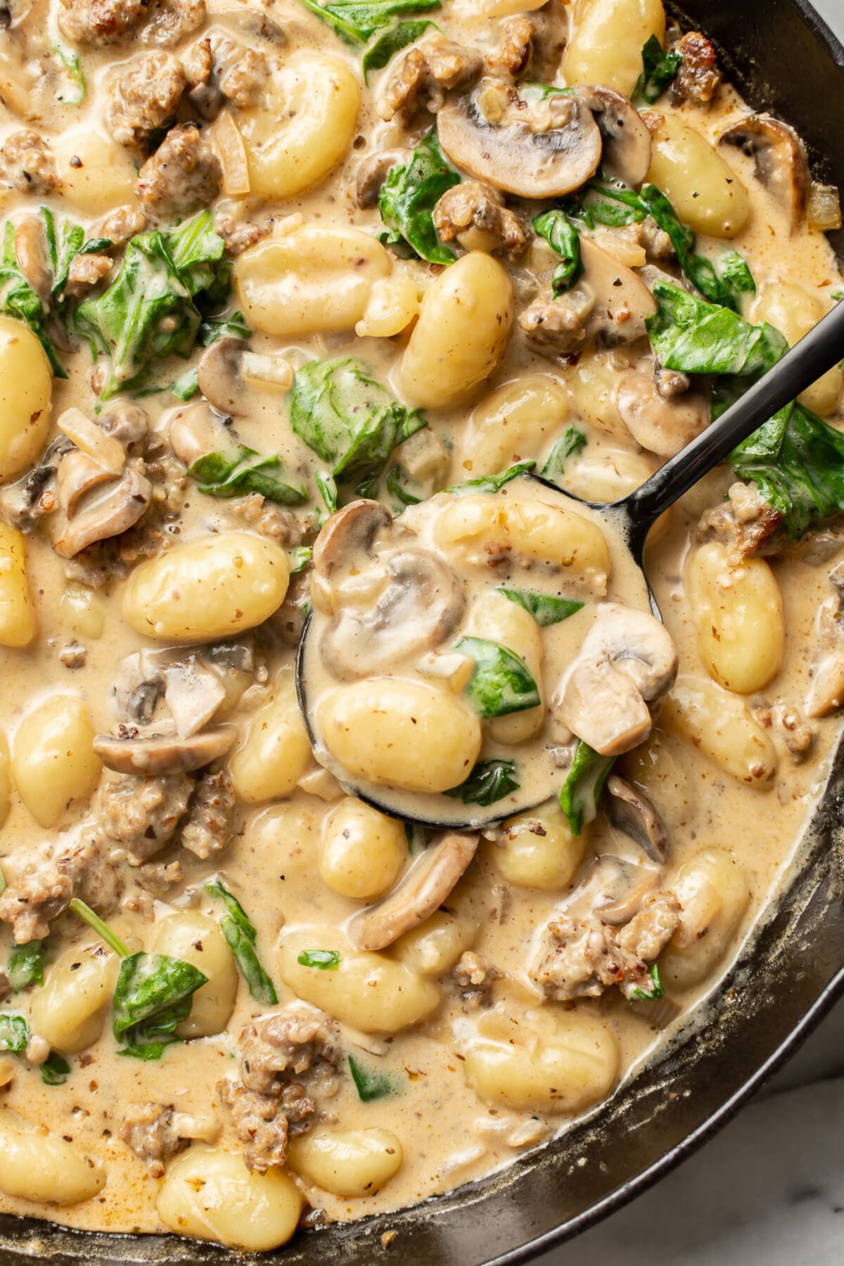 a skillet with italian sausage and mushroom gnocchi with a serving spoon