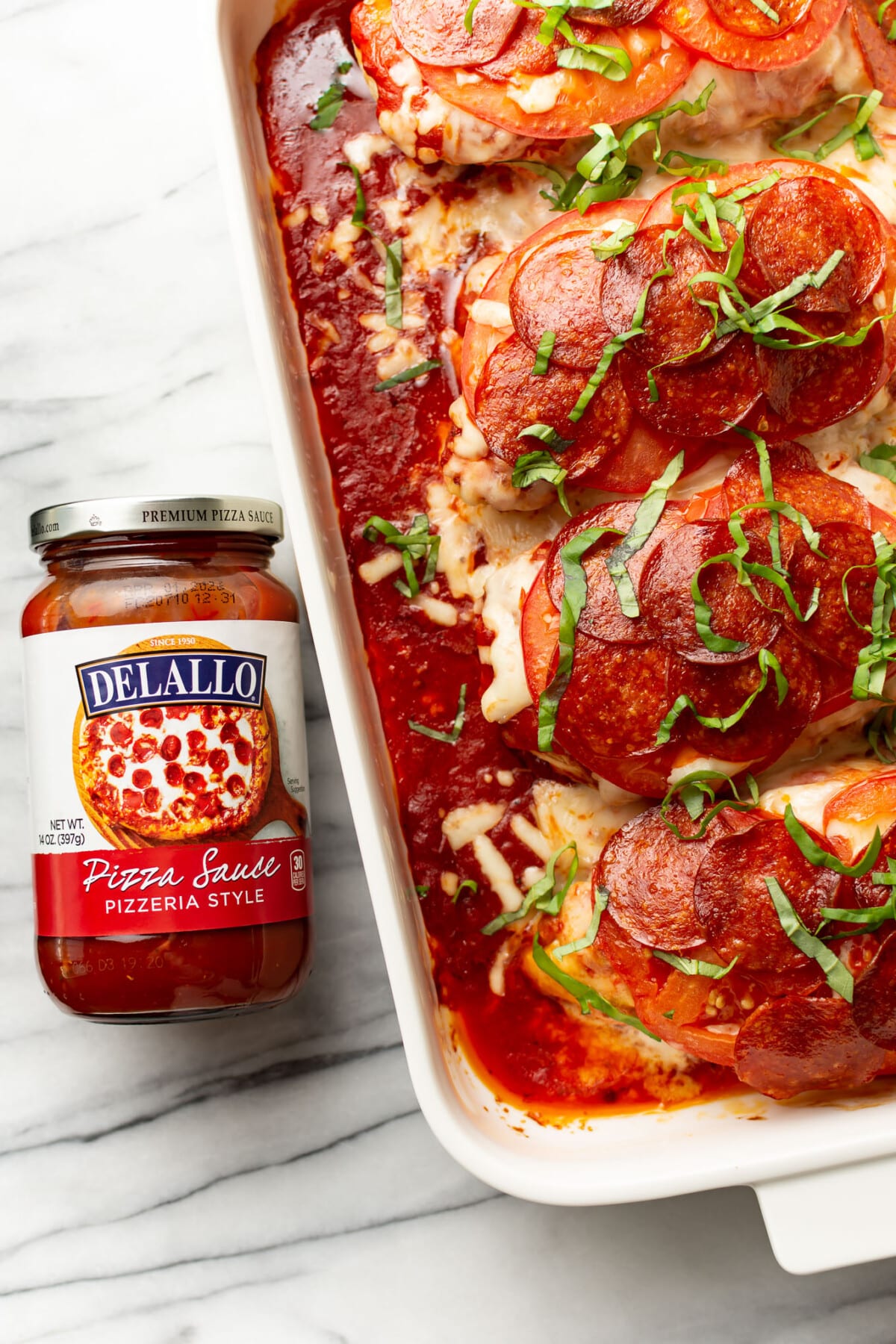 a baking dish with pizza chicken next to a jar of pizza sauce