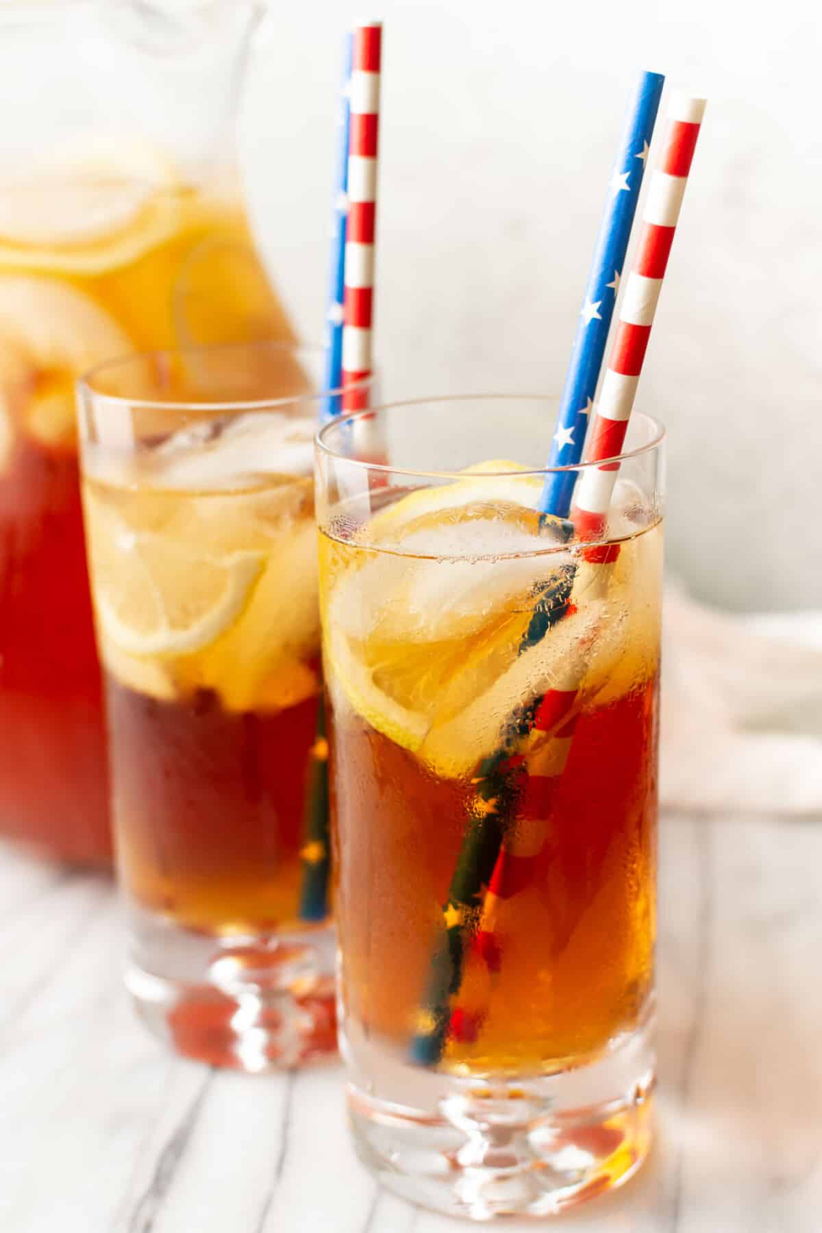 two glasses of sweet tea with lemon in front of a pitcher