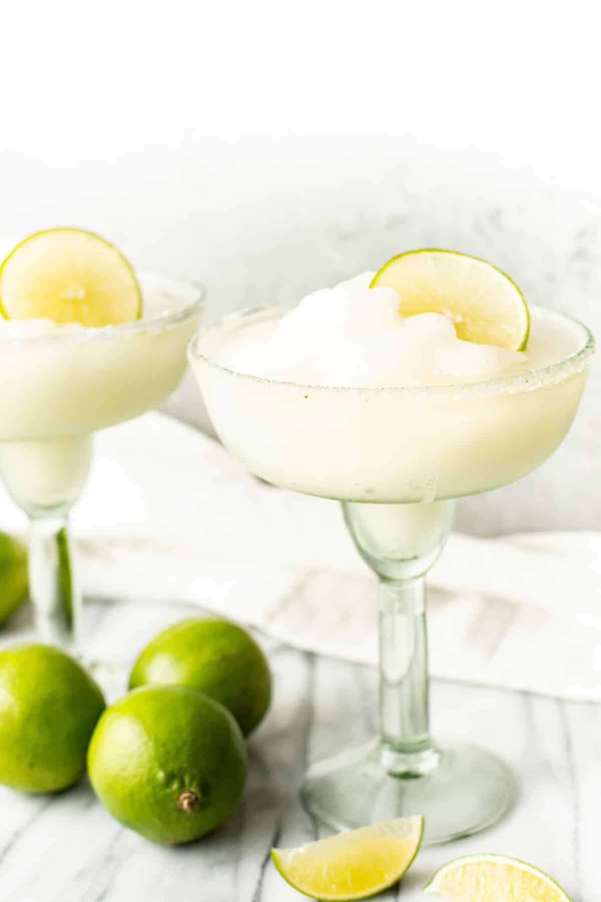 two glasses of frozen margaritas next to limes