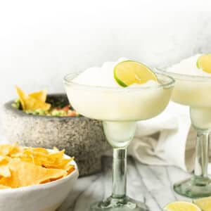 two frozen margaritas next to a bowl of guacamole and chips