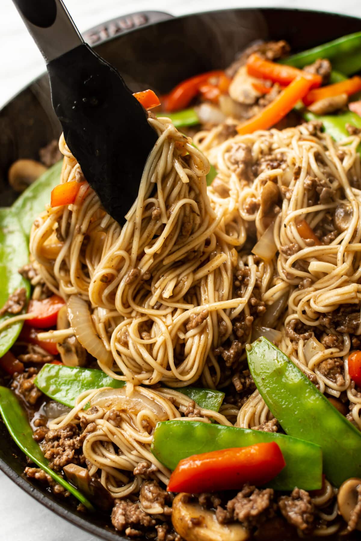 closeup of a skillet with beef lo mein and kitchen tongs