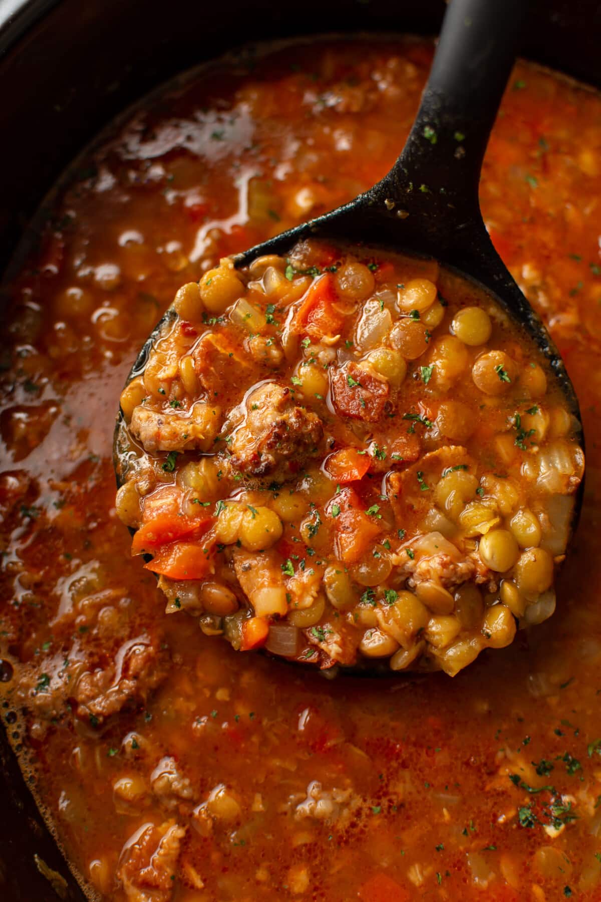 closeup of a slow cooker with sausage and lentil soup and a ladle