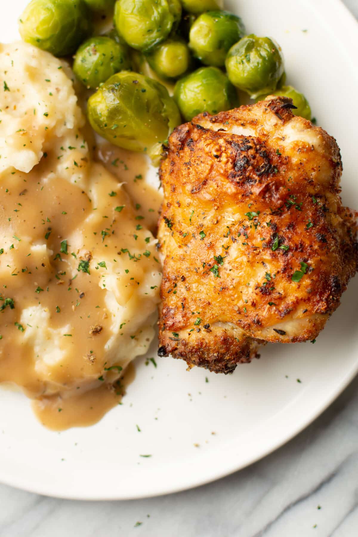 a plate with an air fryer chicken thigh, brussels sprouts, and mashed potatoes with gravy