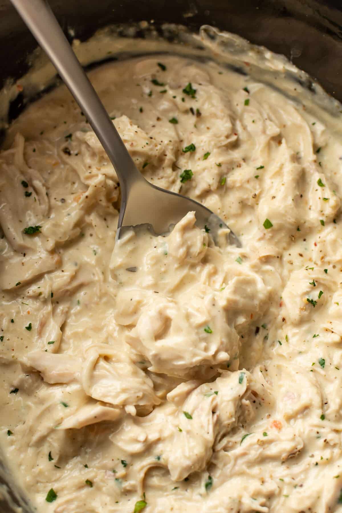 closeup of a slow cooker with italian chicken and a spoon