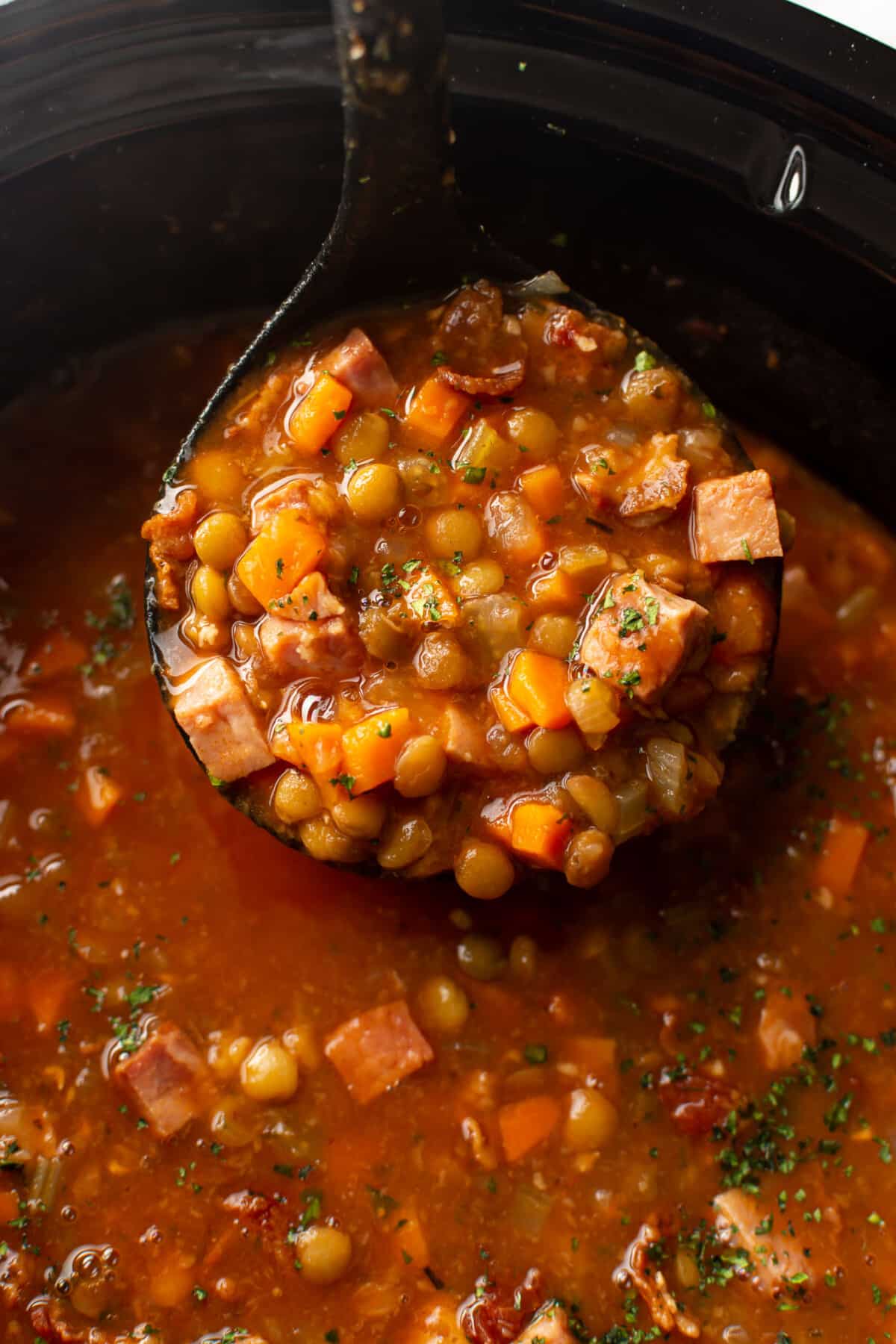 a slow cooker with ham and lentil soup and a ladle