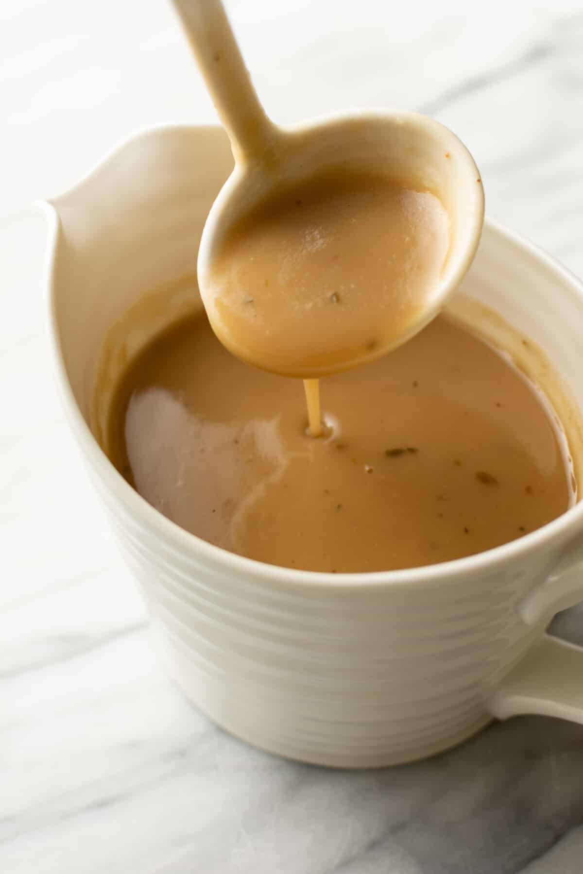 a gravy boat with brown gravy and a serving spoon