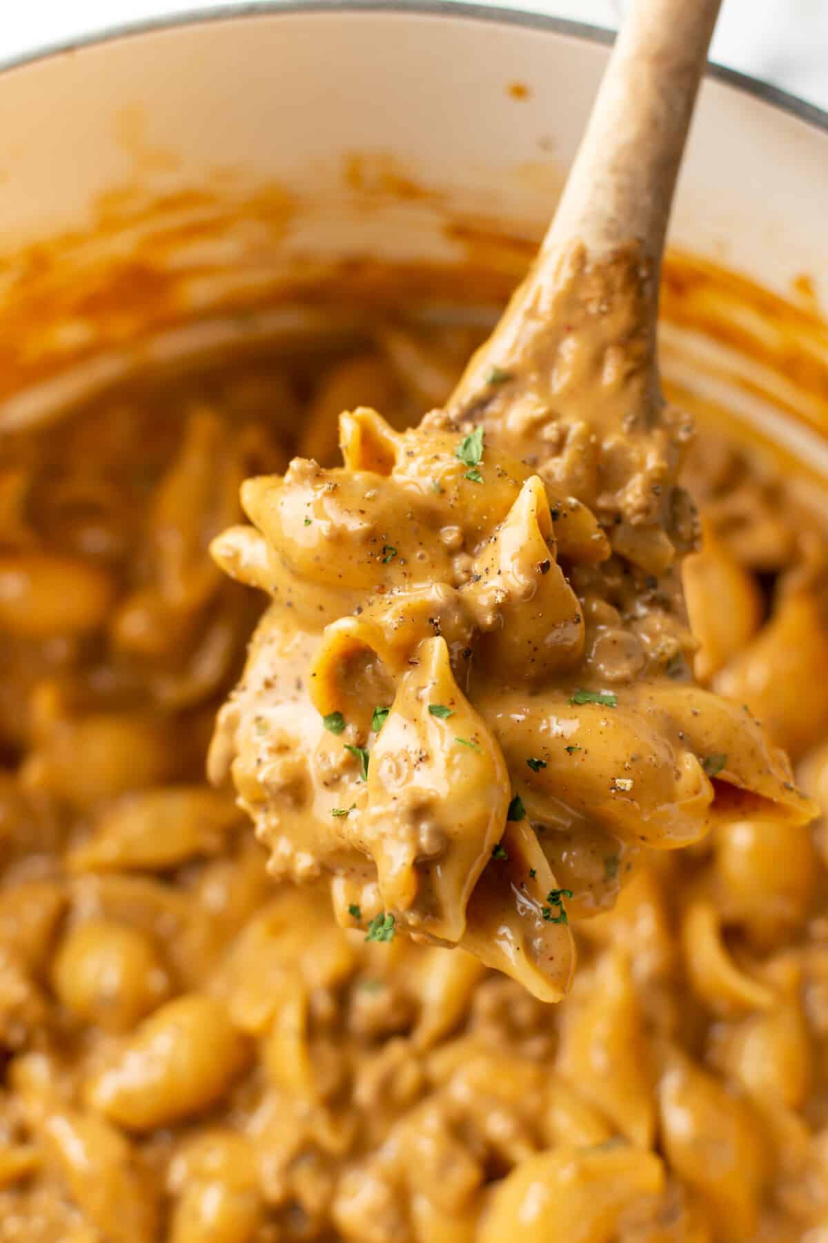 a pot with cheesy beef and shells and a wooden spoon