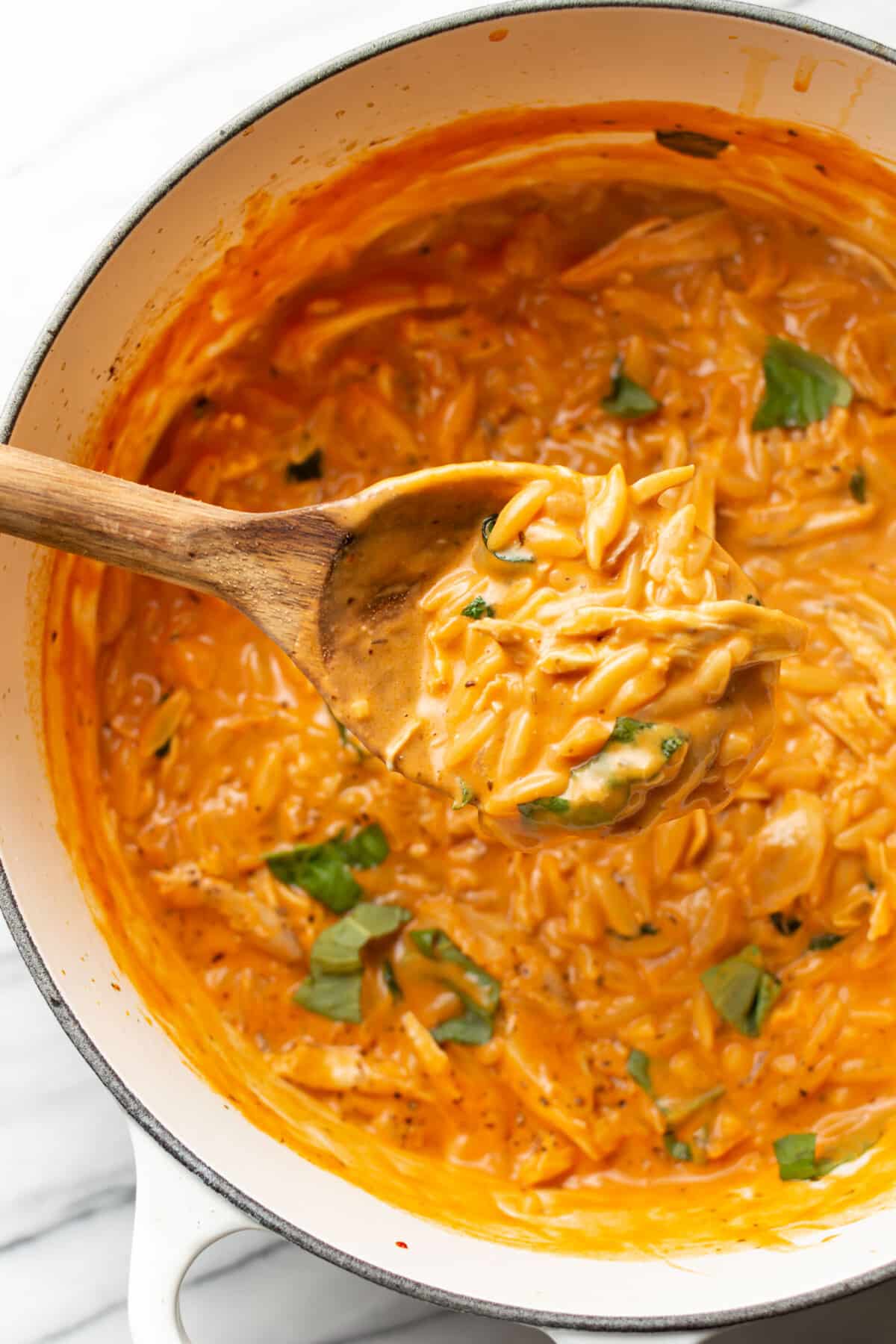 a dutch oven with creamy tomato orzo with chicken and a wooden spoon