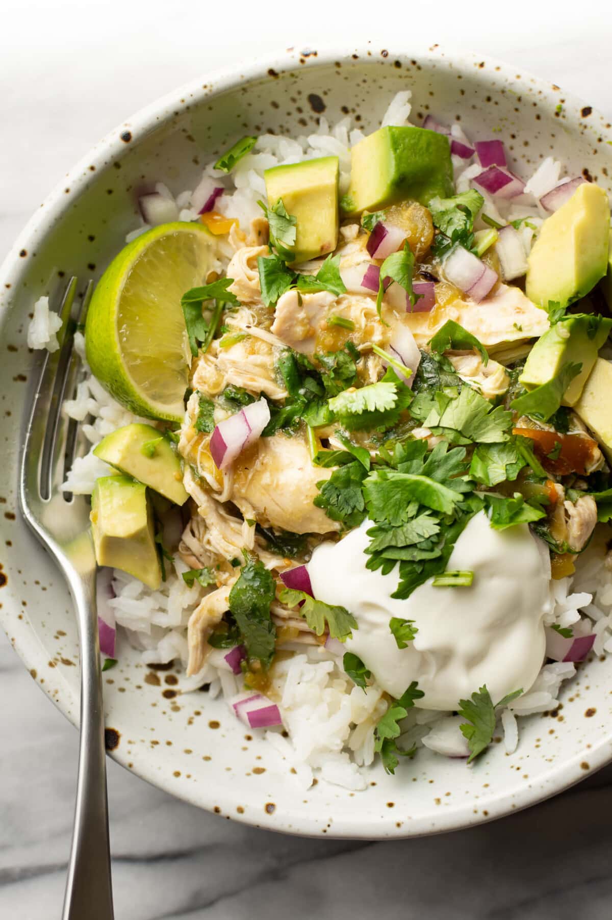 a bowl with crockpot salsa verde chicken over rice and a fork