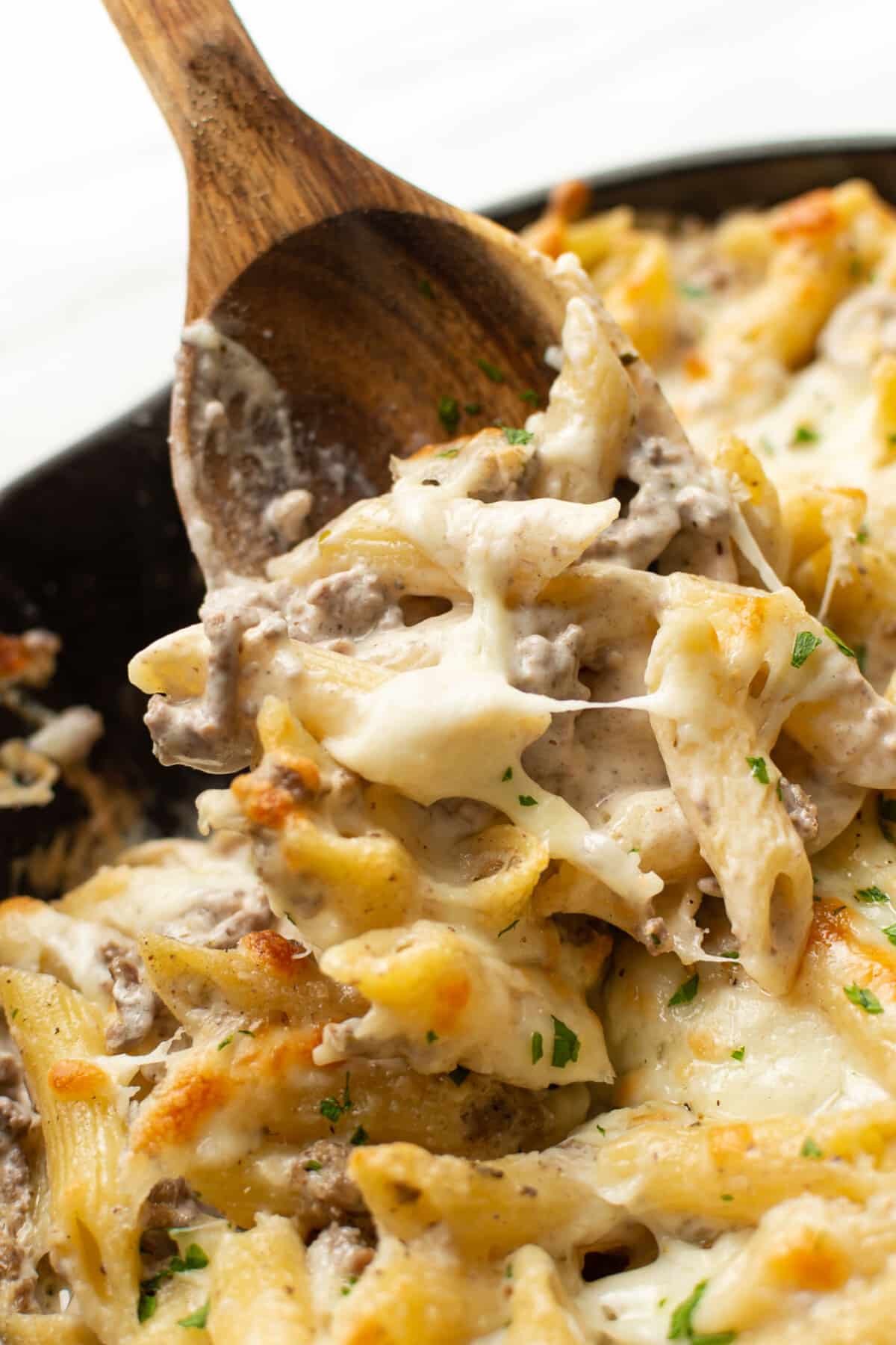 closeup of a skillet with ground beef alfredo bake and a wooden spoon