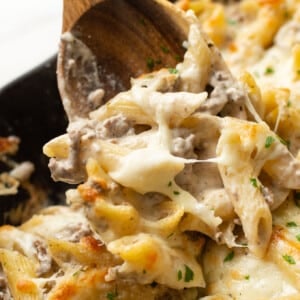 closeup of a skillet with ground beef alfredo bake and a wooden spoon