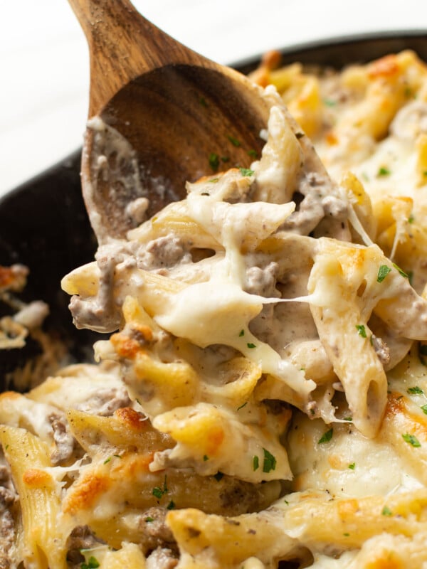 closeup of a skillet with ground beef alfredo bake and a wooden spoon