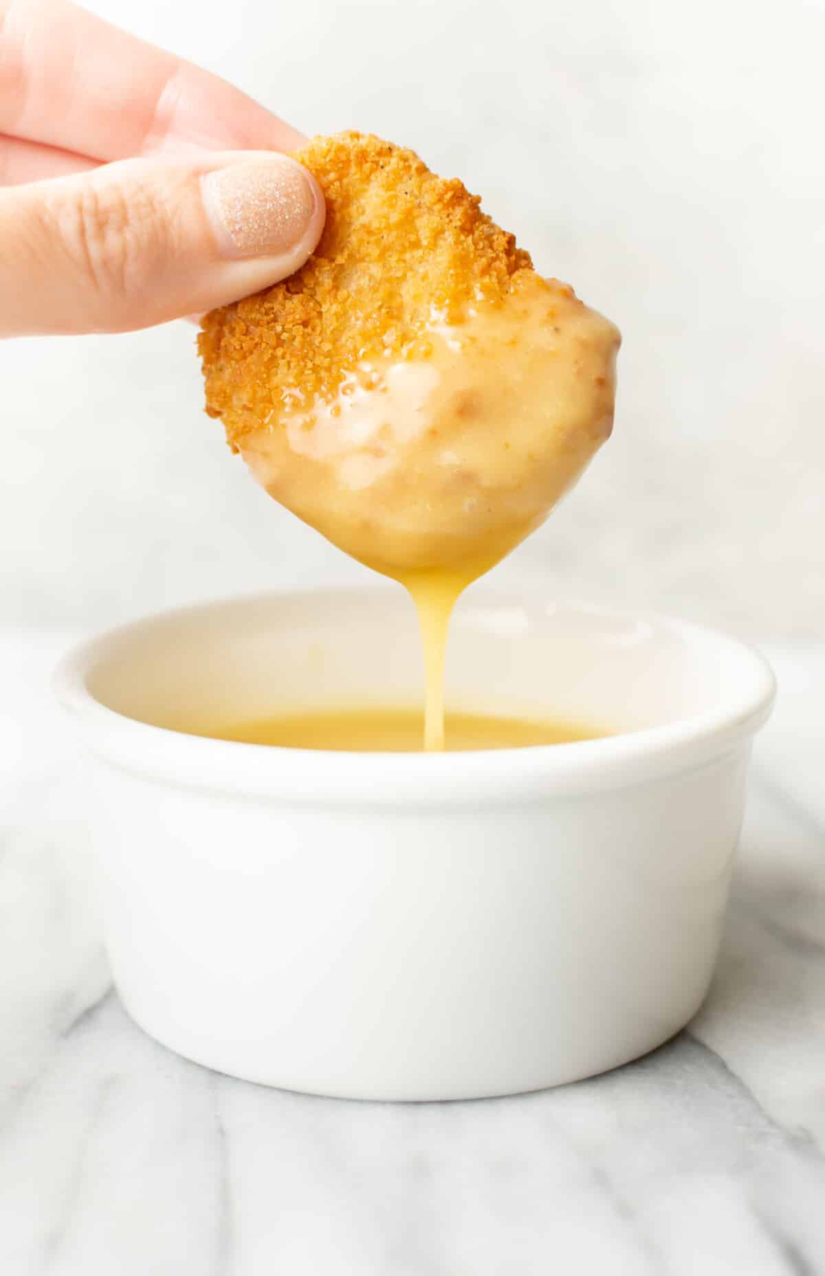 a female hand dipping a chicken nugget into honey mustard dipping sauce