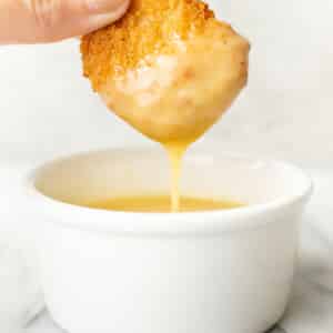 a female hand dipping a chicken nugget into honey mustard dipping sauce